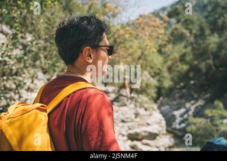 Primo piano vista posteriore del turista maschio adulto che cammina un sentiero di pietra nella foresta di primavera. Ragazzo giovane che indossa abiti casual e zaino giallo durante le escursioni Foto Stock