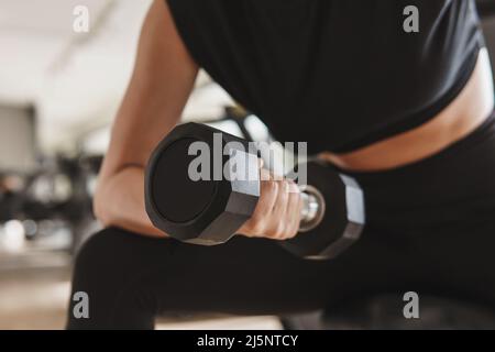 Mano femminile con un manubrio durante l'esercizio di ricciolo in bicipite Foto Stock