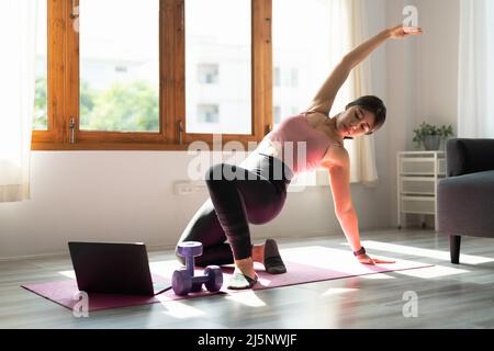 Il giovane addestratore asiatico di idoneità dà la video lezione di yoga mostra l'esercitazione di stretching prima della webcam del laptop in modalità conferenza. Partecipate donne motivate Foto Stock