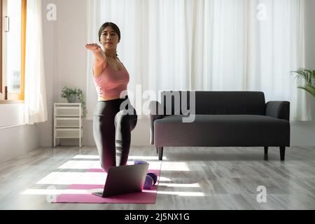 Il giovane addestratore asiatico di idoneità dà la video lezione di yoga mostra l'esercitazione di stretching prima della webcam del laptop in modalità conferenza. Partecipate donne motivate Foto Stock