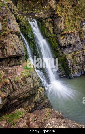 Ad una breve passeggiata attraverso le cime della scogliera da Hartland Quay si trova la cascata di Spoke's Mill Mouth. Le cascate si tuffano a 48 metri dalla cima alla spiaggia sottostante in t Foto Stock