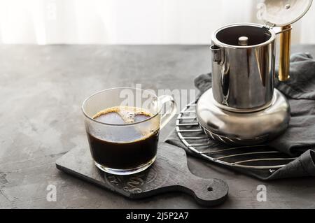 Caffè appena fatto in tazza e caffettiera su sfondo grigio Foto Stock