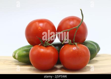 Pomodori rossi freschi e cetrioli verdi disposti su legno con fondo bianco Foto Stock