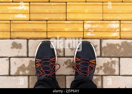 Uomo in piedi alla pavimentazione tattile per handicap cieco. Pavimentazione tattile gialla per non vedenti sul marciapiede. Foto Stock