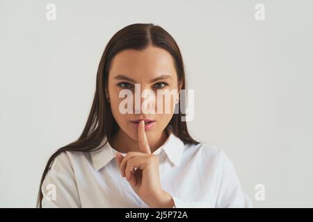 Giovane seria misteriosa ragazza guarda in macchina fotografica e mette il dito sulle labbra chiedendo il silenzio o a Fai silenzio. Gesto shh, concetto segreto. Foto Stock