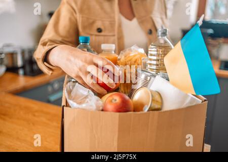 Volontario che confezionano una scatola di carta con aiuti umanitari per i rifugiati ucraini. Concetto di beneficenza, donazione e volontariato Foto Stock