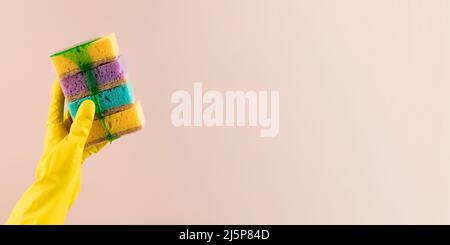 Una mano in un guanto di gomma giallo contiene spugne colorate per i piatti da cui gel. Spazio di copia Foto Stock