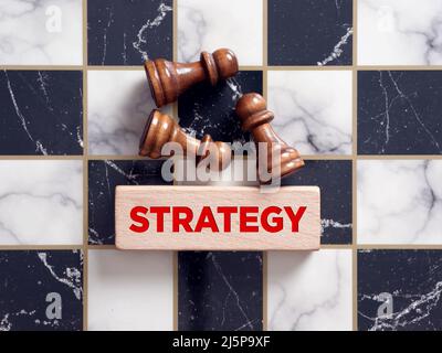 Pedine da scacchi che giacciono sulla scacchiera con la parola strategia su un blocco di legno. Concetto di strategia aziendale. Foto Stock