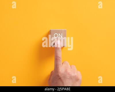 La mano maschio preme su un cubo di legno con la parola sopra. Principio di attivazione dell'avvio aziendale tramite pulsante di accensione. Foto Stock