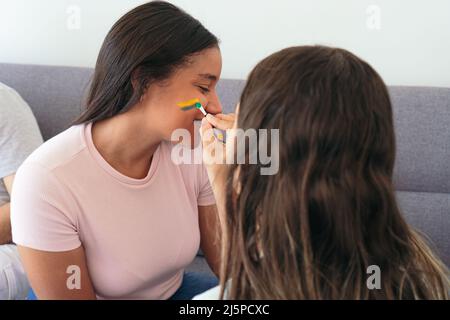 Donna che dipinge la bandiera brasiliana sul volto di un amico Foto Stock