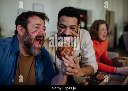 Felici tifosi tedeschi di calcio amici guardare il calcio a casa e mangiare hamburger. Foto Stock