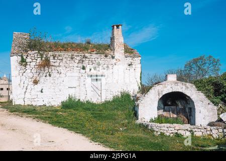 Bel forno o camino in pietra bianca tradizionale nella campagna pugliese, Italia con pareti in pietra asciutta e natura circostante Foto Stock