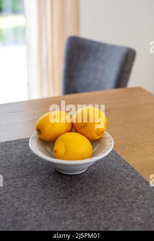 tre limoni in una ciotola su tavola di legno all'interno Foto Stock