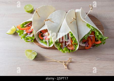 vista frontale di succosi burittos fatti in casa in un focolare con verdure e filetto di pollo. sfondo chiaro in legno Foto Stock