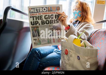 Un passeggero di autobus donna legge la sua copia del giornale Metro il cui titolo in prima pagina riguarda lo scandalo della multa del primo ministro britannico Boris Johnson per la festa durante la pandemia di Covid, quando le sue regole per le riunioni erano proibite, il 22nd aprile 2022, a Londra, Inghilterra. La citazione 'The Gig is Up, Boris' si riferisce al deputato conservatore Steve Baker in parlamento, dicendo a Johnson (attualmente in India) che dovrebbe dimettersi. Si prevede che la polizia MET emetterà più multe a pena fissa per le parti illegali che hanno volato Johnson a Downing Street. Foto Stock