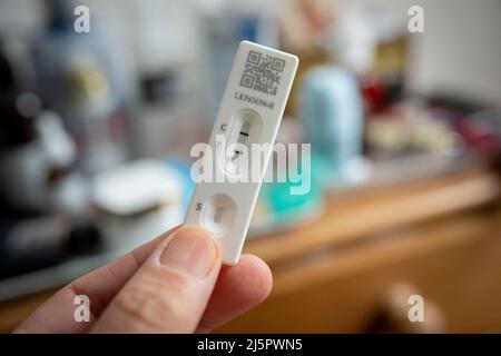 Un dettaglio di una mano che tiene un test di flusso laterale che mostra un risultato positivo in una camera da letto domestica, il 23rd aprile 2022, a Londra, Inghilterra. Foto Stock