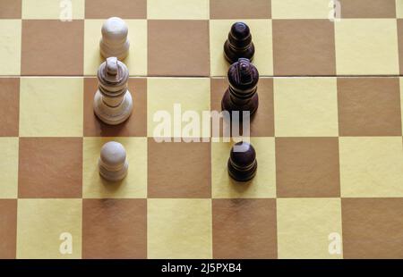 Il re bianco e le due pedine di fronte ai pezzi di scacchi marroni sulla scacchiera Foto Stock