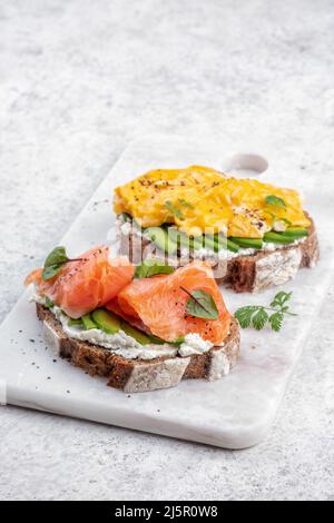 Uova strapazzate con salmone affumicato, formaggio spalmabile e avocado su pane tostato Foto Stock