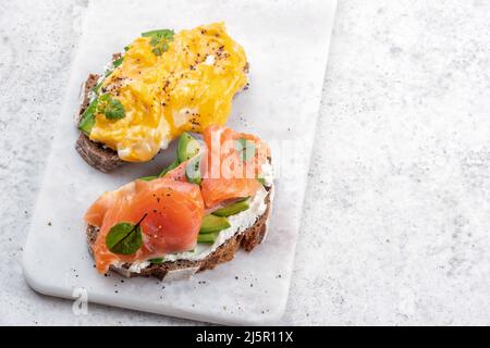 Uova strapazzate con salmone affumicato, formaggio spalmabile e avocado su pane tostato Foto Stock