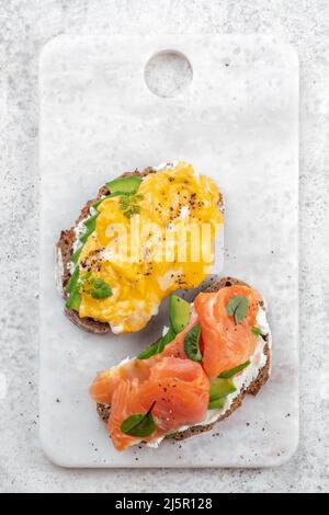 Uova strapazzate con salmone affumicato, formaggio spalmabile e avocado su pane tostato Foto Stock