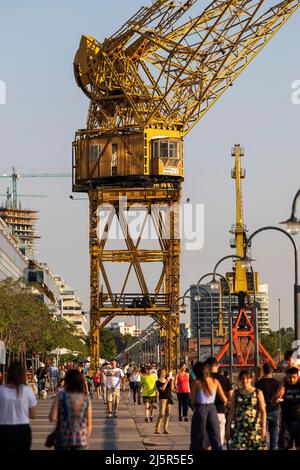 Argentina, Buenos Aires - a Puerto Madero la gente sta passeggiando sul viale lungo le vecchie gru, caffè, il ponte e vecchie barche a vela. Foto Stock