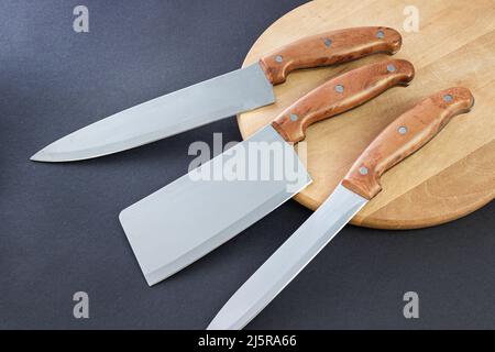 Coltello da cucina su cemento e asse di legno. Collezione di vari coltelli da cucina. Foto Stock