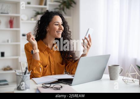 Donna del Medio Oriente allegra che usa il cellulare seduto sul posto di lavoro Foto Stock