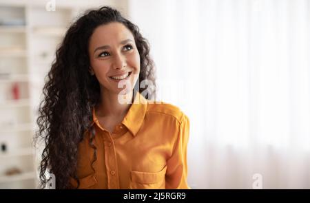 Felice Brunette Lady in posa guardando da parte sorridente in piedi a casa Foto Stock