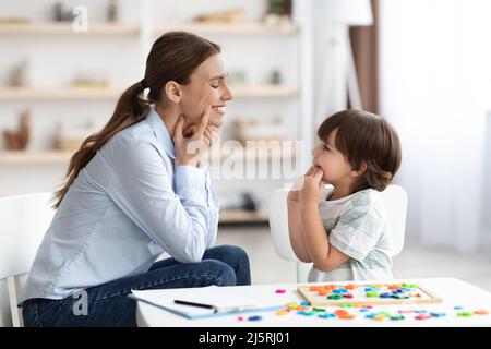 Professionale donna specialista di formazione con ragazzo carino, mostrando lui esercizio orale per riscaldare i muscoli della bocca Foto Stock