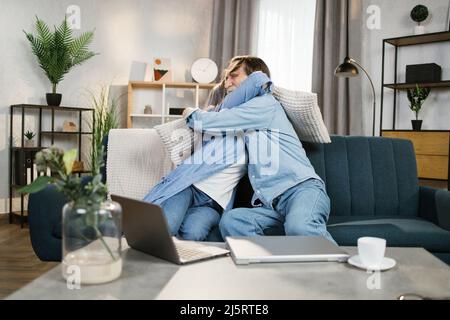 Coppia di due anziani felici divertirsi giocando insieme sul divano a casa si abbracciano dopo aver combattuto con i cuscini godendo - guanciali guerra al coperto al mattino. Foto Stock