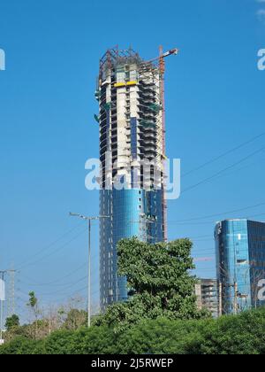 ingrandisci la foto di un edificio alto a più piani in fase di costruzione, parzialmente realizzato con una gru sopra di esso con un aeroplano che passa dietro Foto Stock