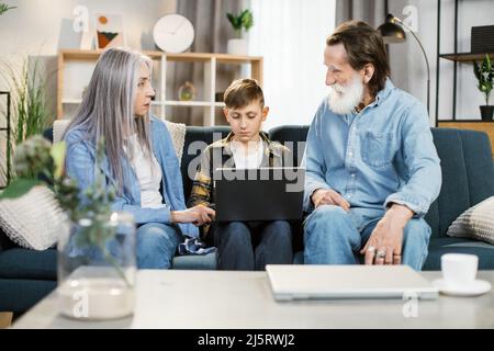 Nipote insegnare anziano a navigare in internet utilizzando il computer e la tecnologia e lo stile di vita moderno. Buon nonno caucasico con nipote seduto sul divano giocare insieme il computer portatile a casa Foto Stock
