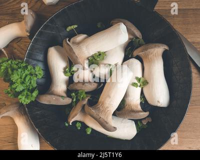 Funghi freschi di ostriche - Pleurotus eryngii in padella di ferro su un tavolo da cucina in legno vista dall'alto Foto Stock