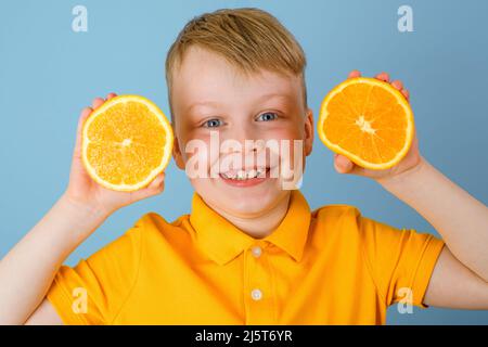 Ritratto bambino allegro tenendo due metà di un arancio con le sue mani. Emozioni positive. Isolato su sfondo blu. Bambino in t-shirt gialla. Q. Alta Foto Stock