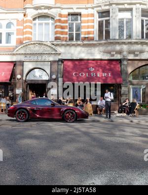 Londra, Greater London, Inghilterra, Aprile 16 2022: Porsche viola parcheggiata fuori Colbert, un ristorante francese a Sloane Square con una tenda viola. Foto Stock