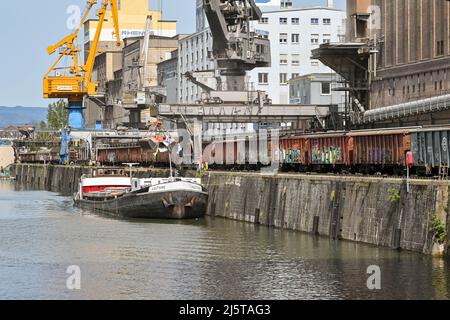 Basilea, Svizzera - Aprile 2022: La chiatta industriale che trasporta la sabbia viene scaricata da una gru nel porto della città sul fiume Reno Foto Stock