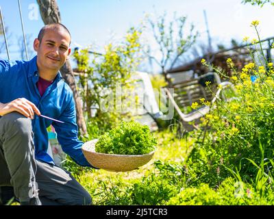 il giovane uomo felice raccoglie un cestino di verdure nel suo orto in città Foto Stock