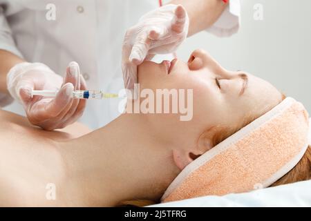 Il cosmetologo esegue la procedura di sollevamento del mento iniettando le iniezioni di bellezza. Medico iniettando acido ialuronico nel ching di una donna come un viso Foto Stock