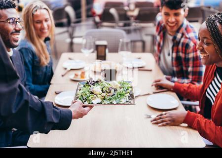 cameriere che serve un'insalata a clienti multietnici su una terrazza ristorante Foto Stock