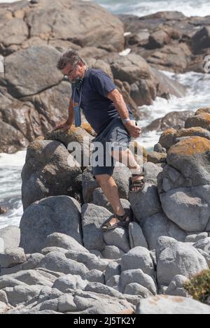 Costa occidentale, Sudafrica. 2022. Uomo che si arrampica sulle rocce in una località balneare sulla costa occidentale, Sudafrica Foto Stock