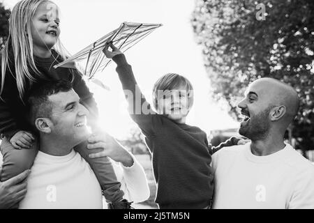 Gay coppia maschile e bambini divertirsi con il giocattolo kite outdoor - LGBT famiglia e amore concetto - Focus on left father face - editing in bianco e nero Foto Stock