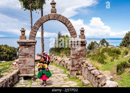 Una madre Taquileno e bambino camminando lungo il percorso dal porto alla città, Taquile Island, Lago Titicaca, Puno, Perù. Foto Stock