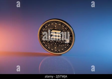 Solana Sol Cryptocurrency moneta fisica posta su superficie riflettente e illuminata con luci arancione e blu. Scatto macro. Messa a fuoco selettiva. Foto Stock