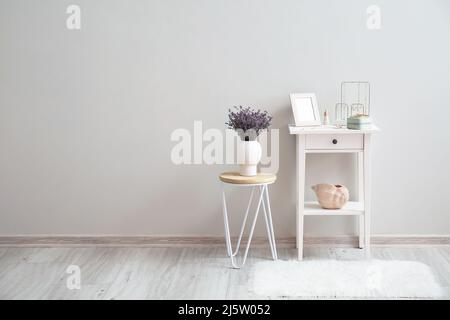 Tavolo con gioielli eleganti e vaso con fiori vicino alla parete luminosa in camera Foto Stock