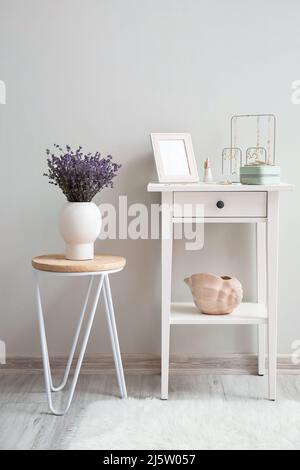 Tavolo con gioielli alla moda e vaso con fiori vicino alla parete luminosa in camera Foto Stock