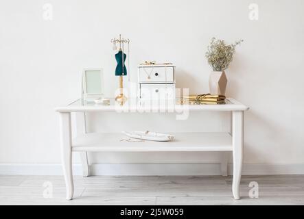 Gioielli alla moda, vaso con fiori e cornice fotografica sul tavolo vicino alla parete bianca Foto Stock