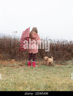 Una ragazza giovane che indossa stivali da pioggia e cappotto che regge un look ombrello Foto Stock