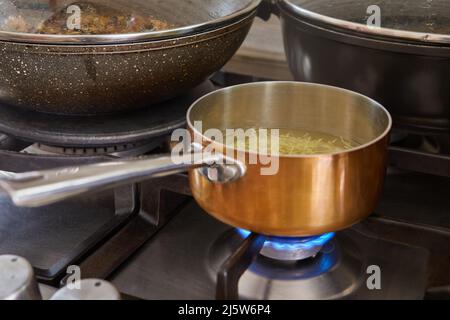 Pentola con manico in rame e acciaio inox su fuoco di stufa a gas Foto Stock