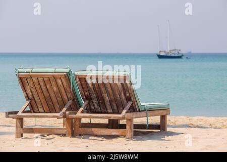 Due sedie a sdraio in legno su una spiaggia di sabbia tropicale che si affaccia sul mare e yacht. Thailandia. Primo piano. Concetto di vacanza ed estate Foto Stock