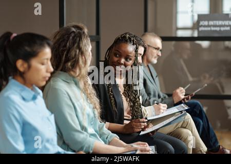 Giovane ragazza africana che parla con la donna mentre si siedono in coda per l'intervista di lavoro e la compilazione dei documenti Foto Stock